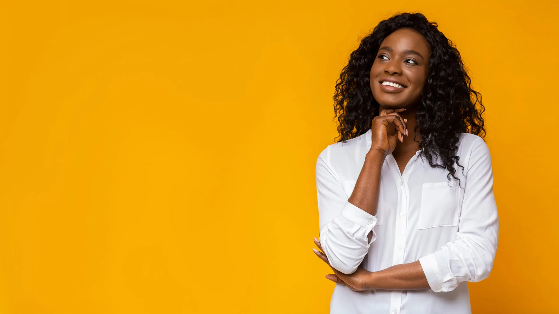 Femme aux cheveux bouclés en chemise blanche souriante sur un fond jaune